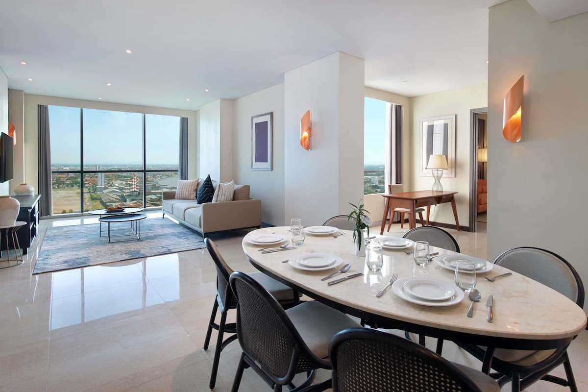 A modern hotel room with a dining area, a sofa, and a view of the city.