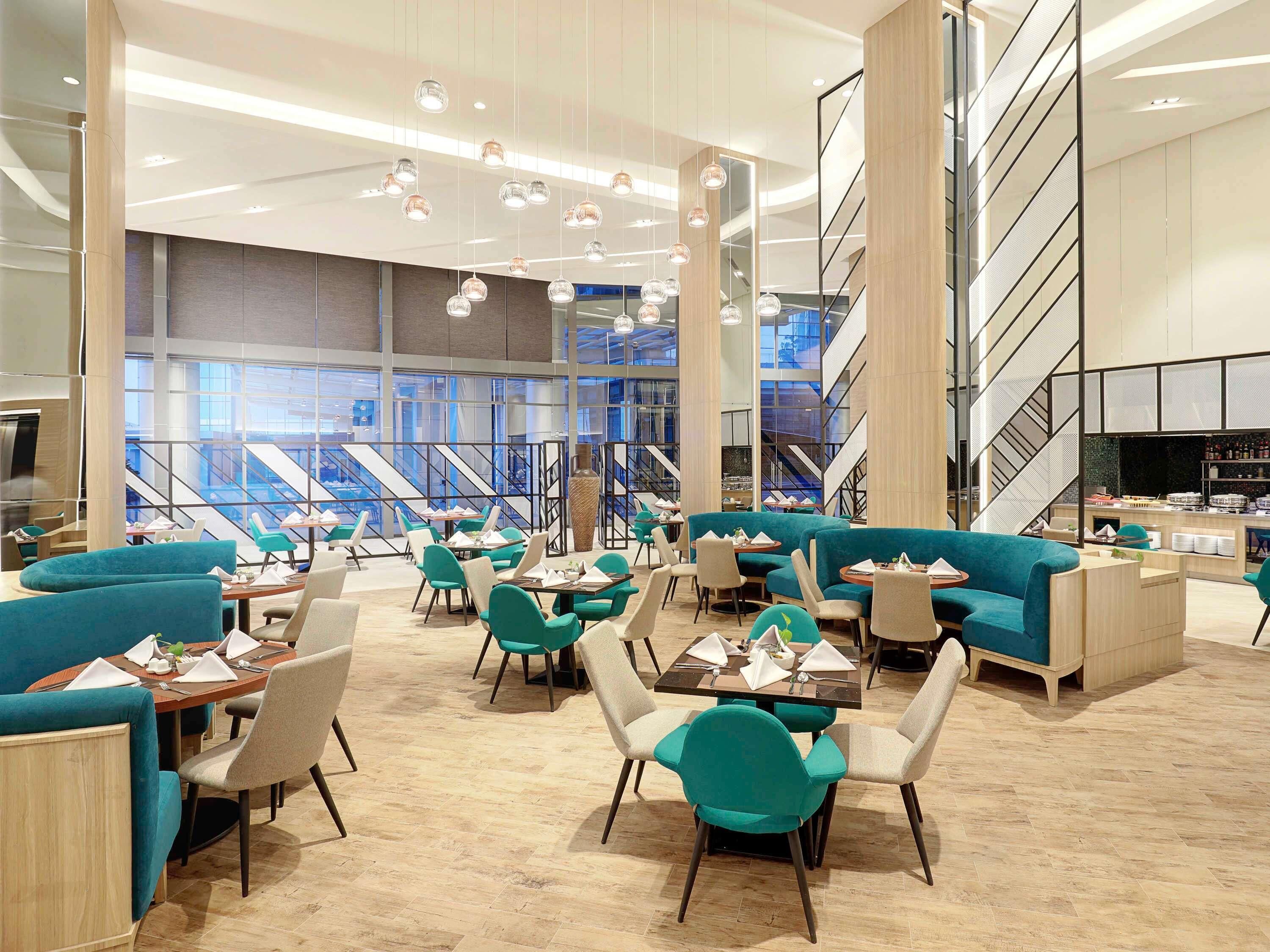 A modern dining area with teal upholstered seating, wooden tables, and hanging pendant lights.