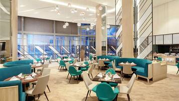 A modern dining area with teal upholstered seating, wooden tables, and hanging pendant lights.