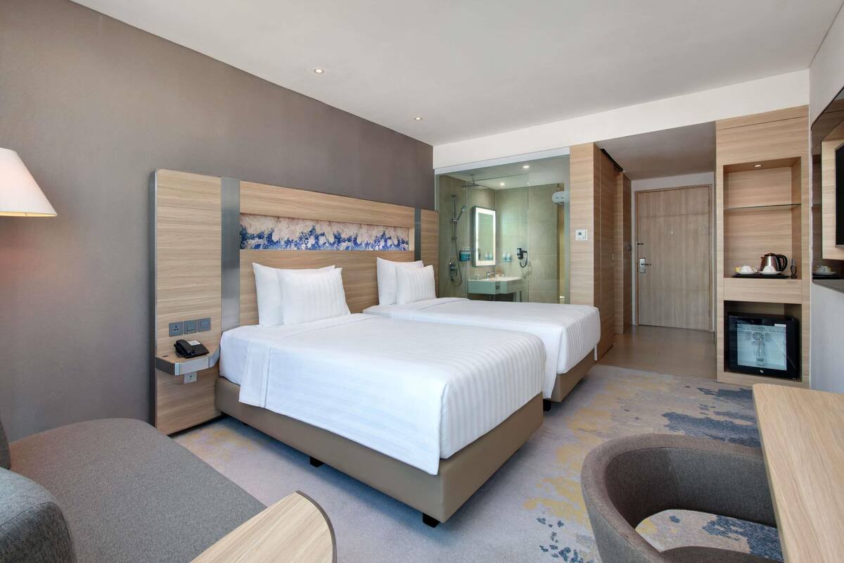 A hotel room with two beds, a desk, a chair, a bathroom, and a TV.