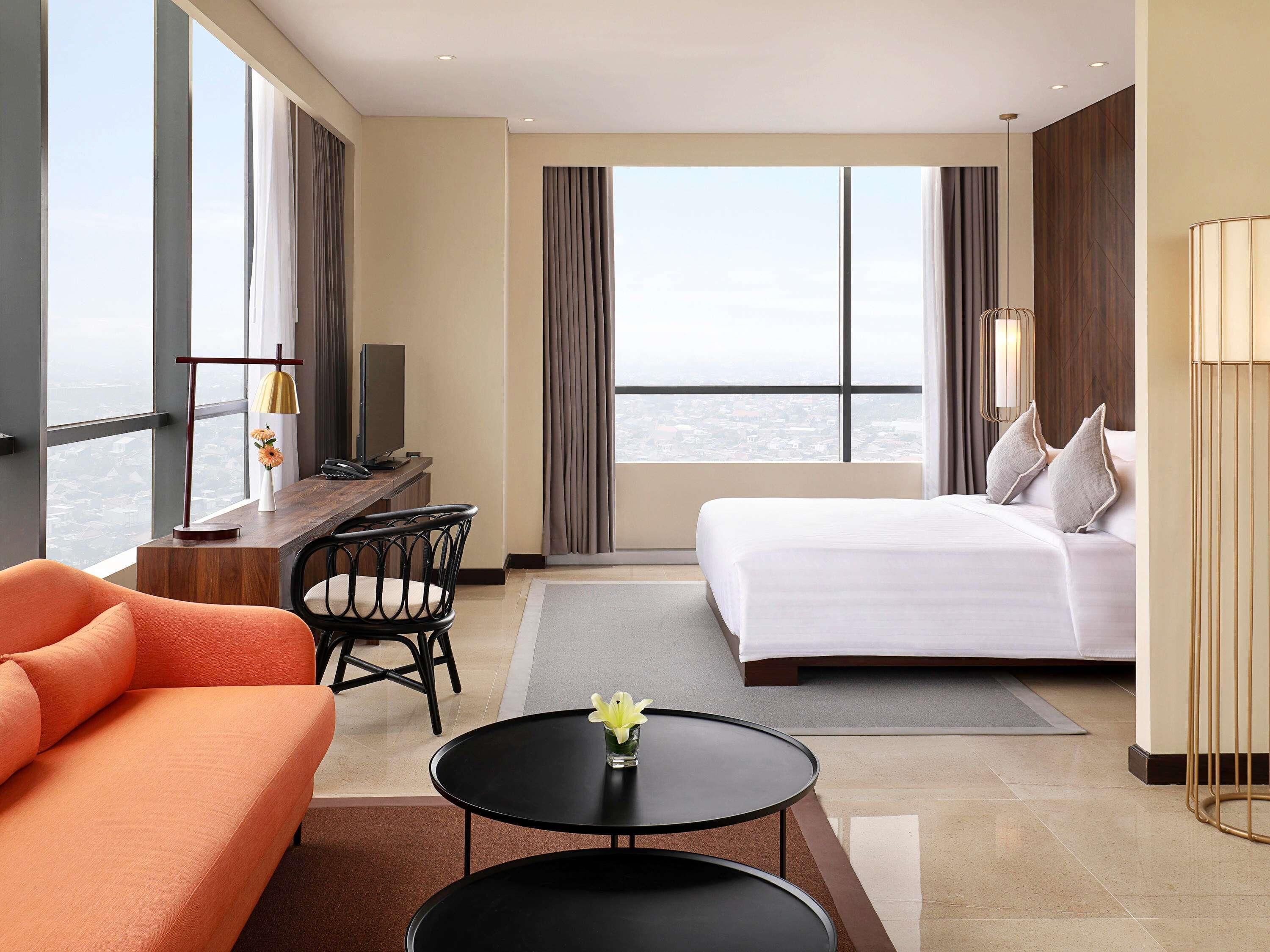 A hotel room with a bed, a desk, a chair, a sofa, and a view of the city.