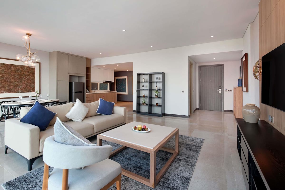 A modern living room with a sofa, coffee table, and a dining area with a kitchen in the background.