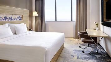 Habitación de hotel con una cama grande, un escritorio, una silla, una lámpara y un televisor.
