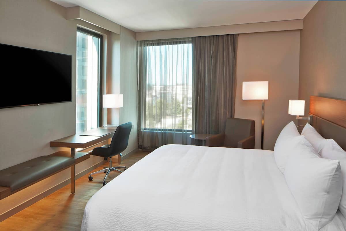 A hotel room with a large bed, a desk with a chair, a television mounted on the wall, and a window with curtains.