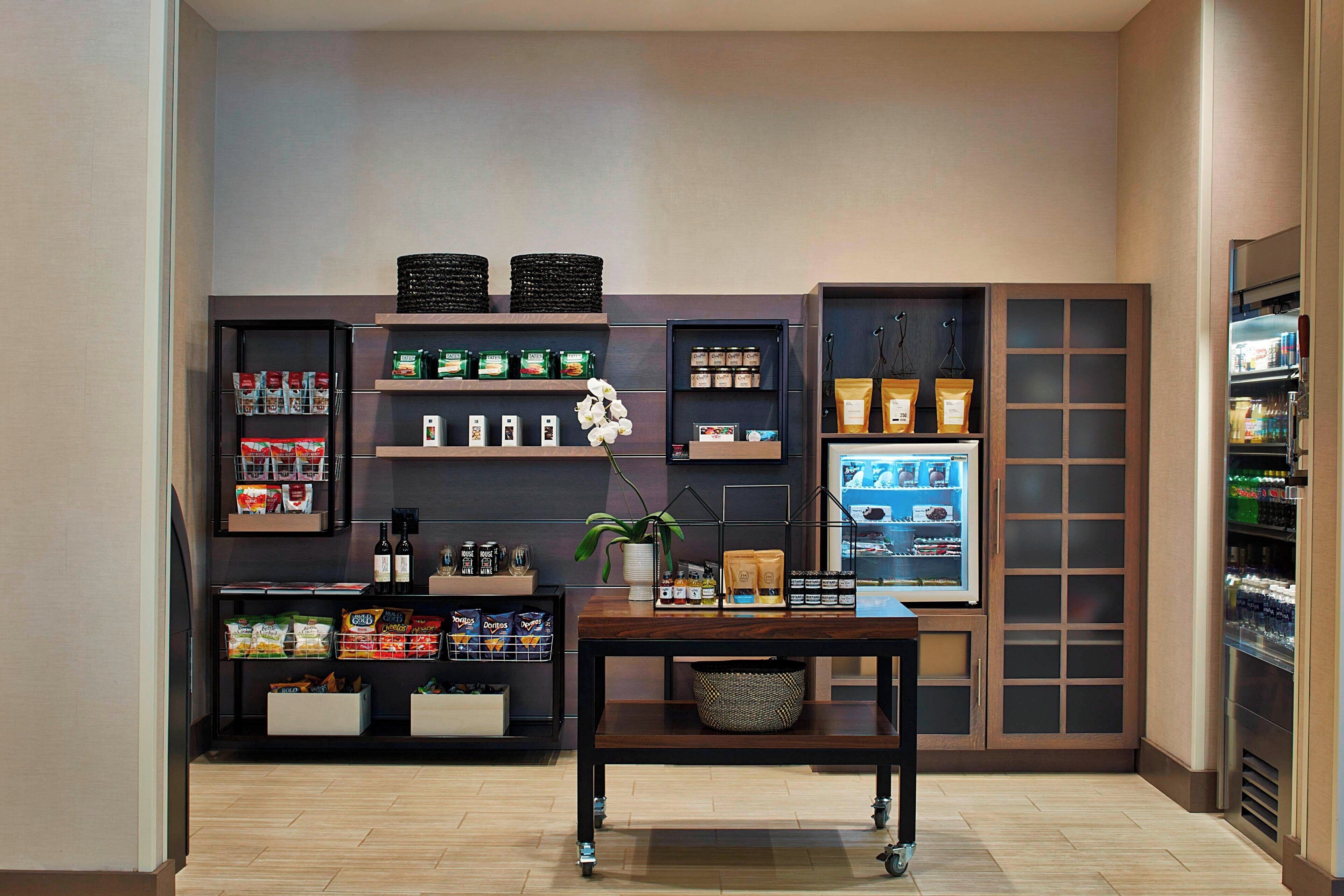 A modern kitchen with built-in appliances, shelves stocked with snacks and condiments, and a central island with a basket.