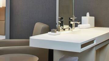 A modern bathroom with a white sink, a large mirror, a towel rack with folded towels, and a round table.