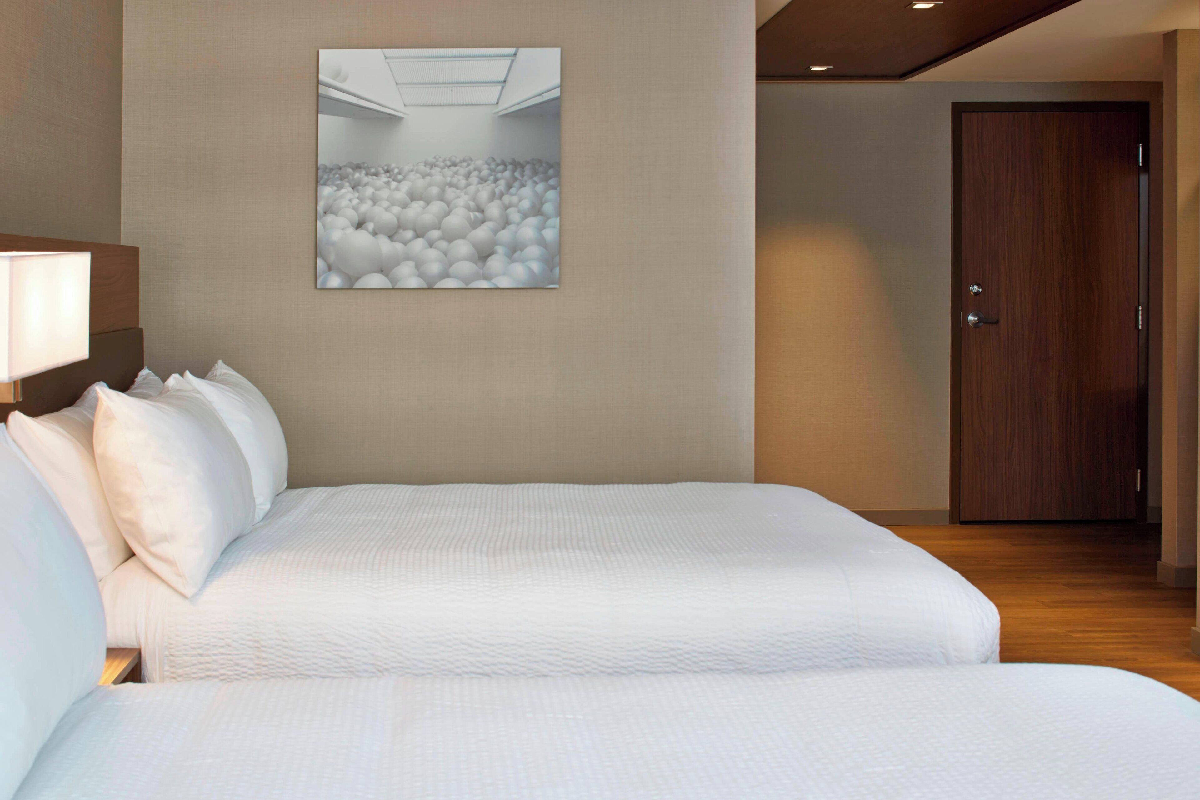 Habitación de hotel con una cama grande, cabecera, un cuadro colgado en la pared y una puerta de madera.