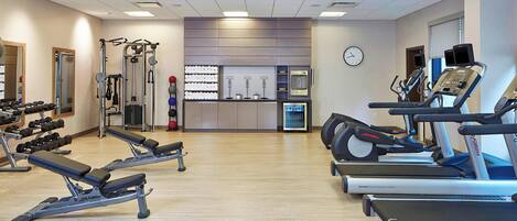 A gym with cardio machines, weightlifting equipment, and a wall-mounted clock.