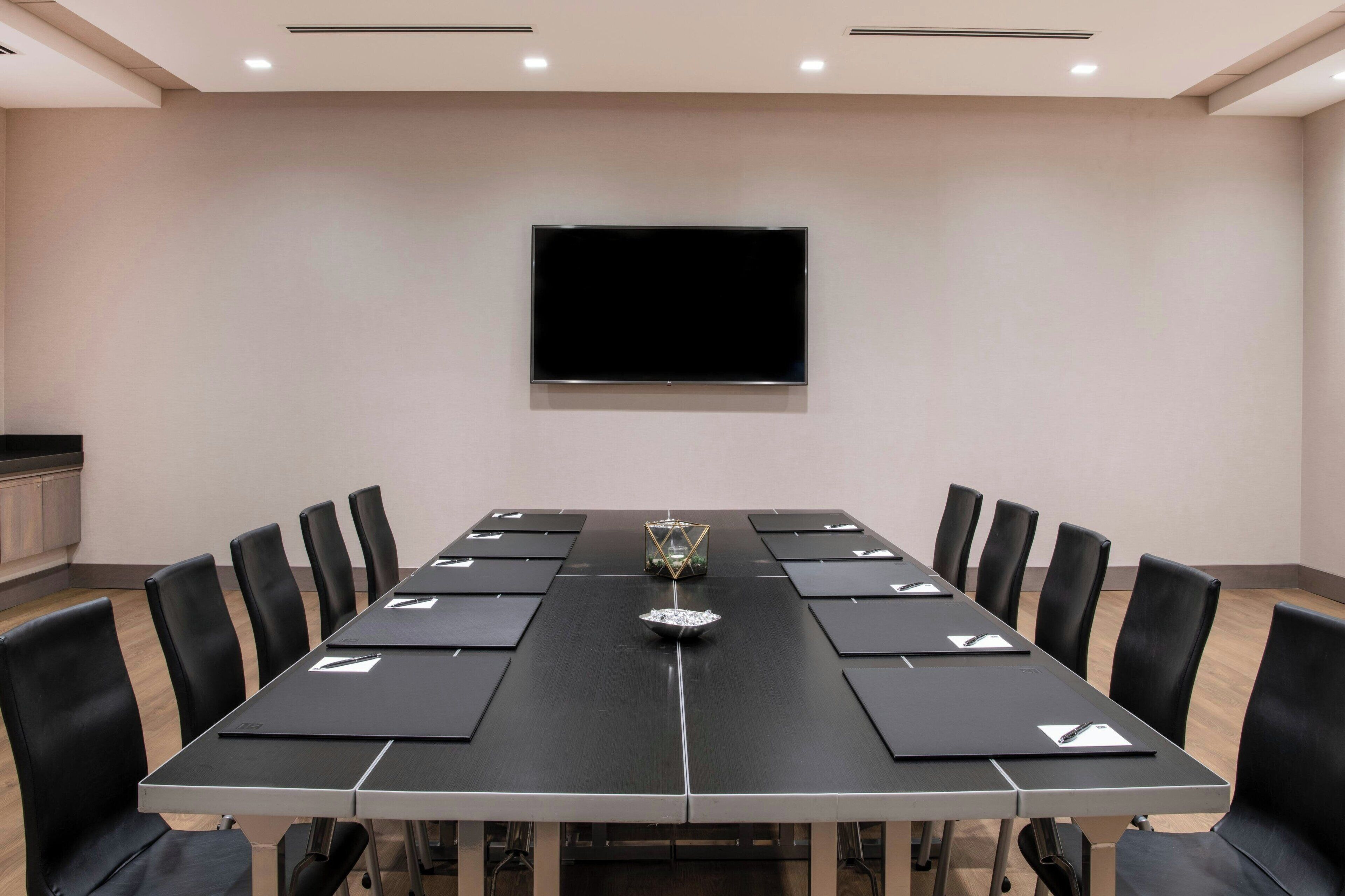 A conference room with a long table, black chairs, and a flat-screen TV on the wall.