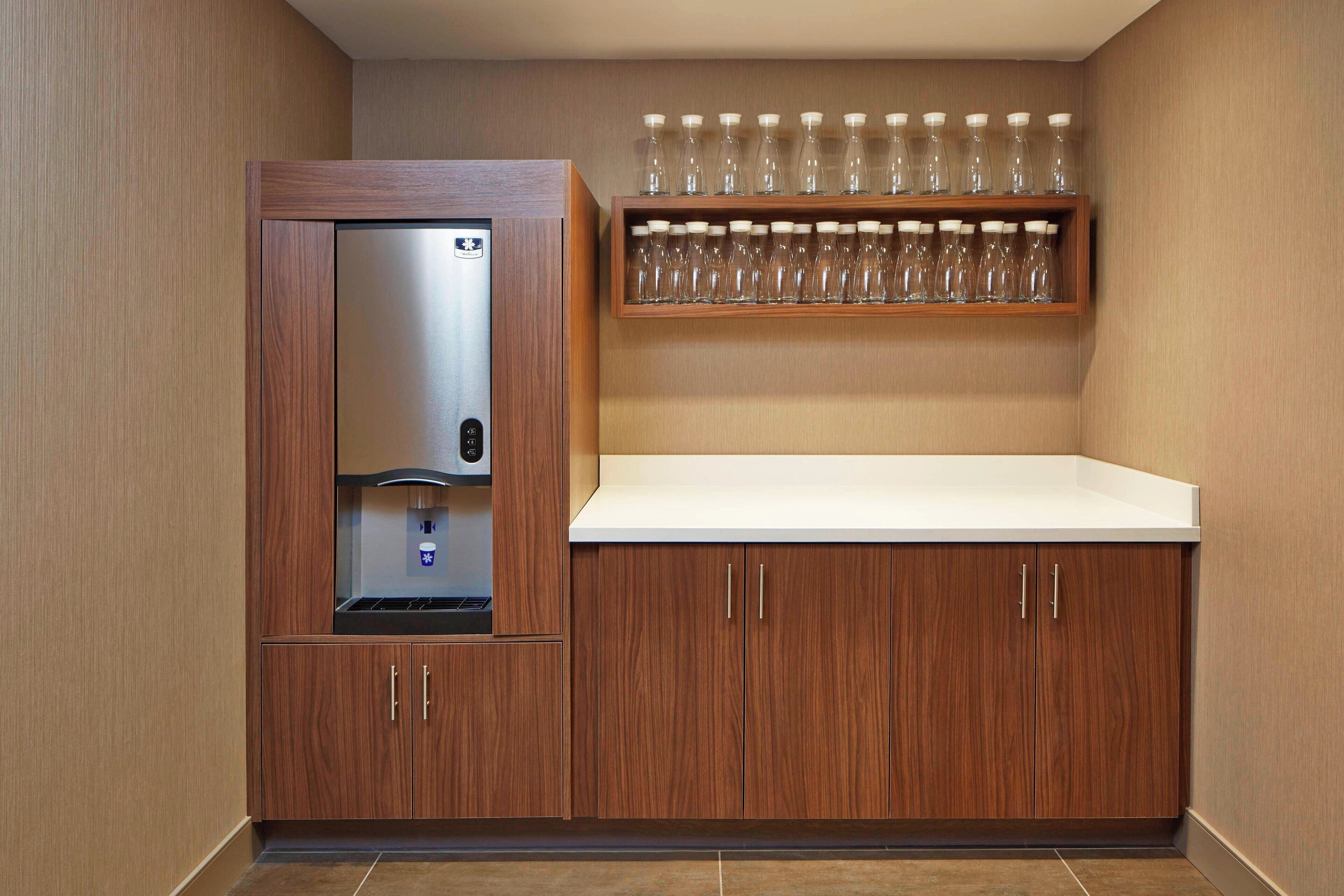 A kitchenette with a built-in refrigerator, a microwave, and a shelf with multiple glasses.