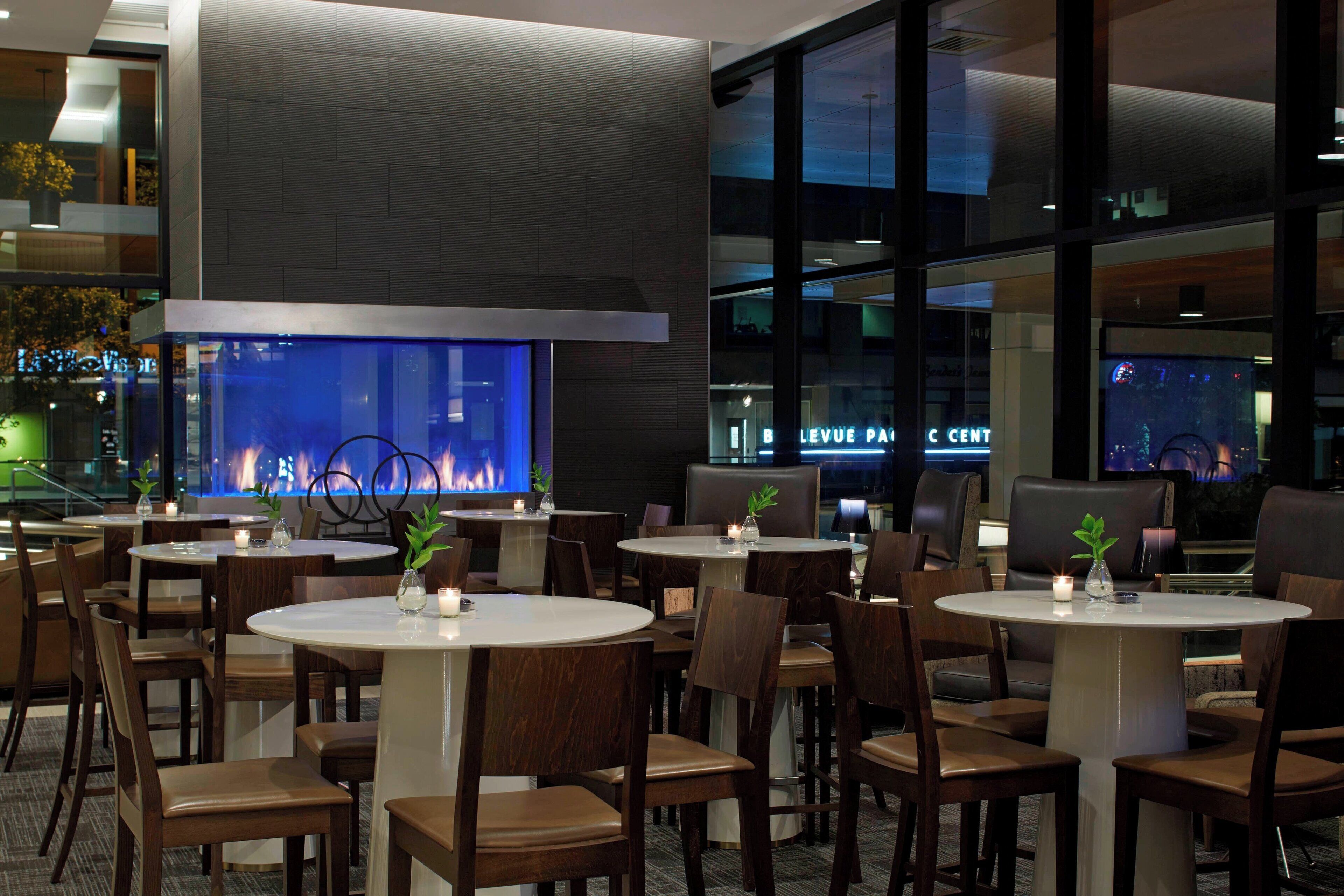 Un restaurant moderne avec des tables et des chaises rondes, un grand écran de télévision et une cheminée.