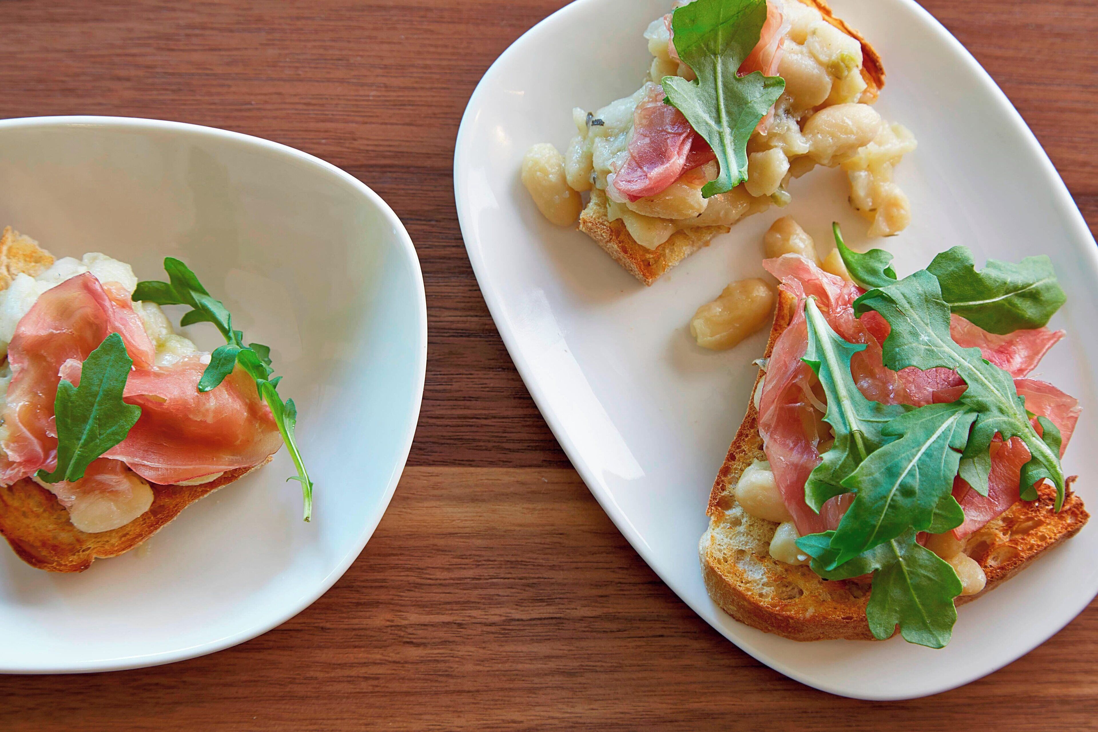 Dos platos de bruschetta con rúcula y prosciutto.