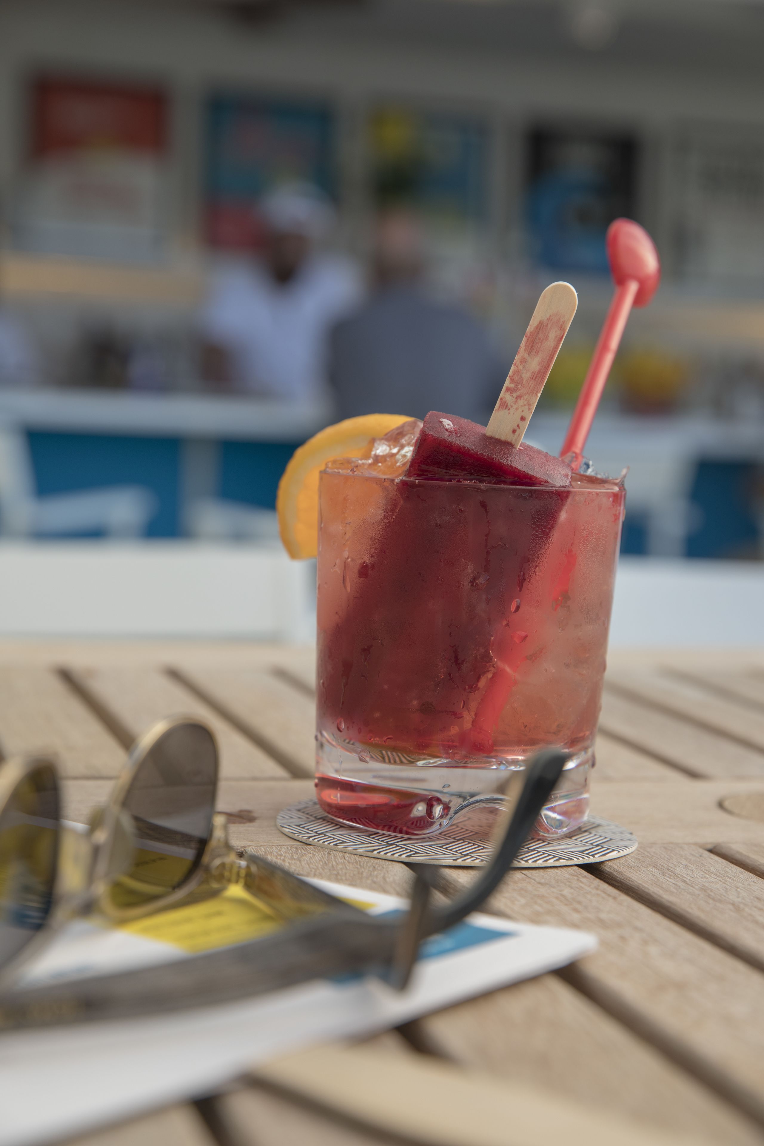 A glass of iced drink with a straw and a slice of fruit on a wooden table.