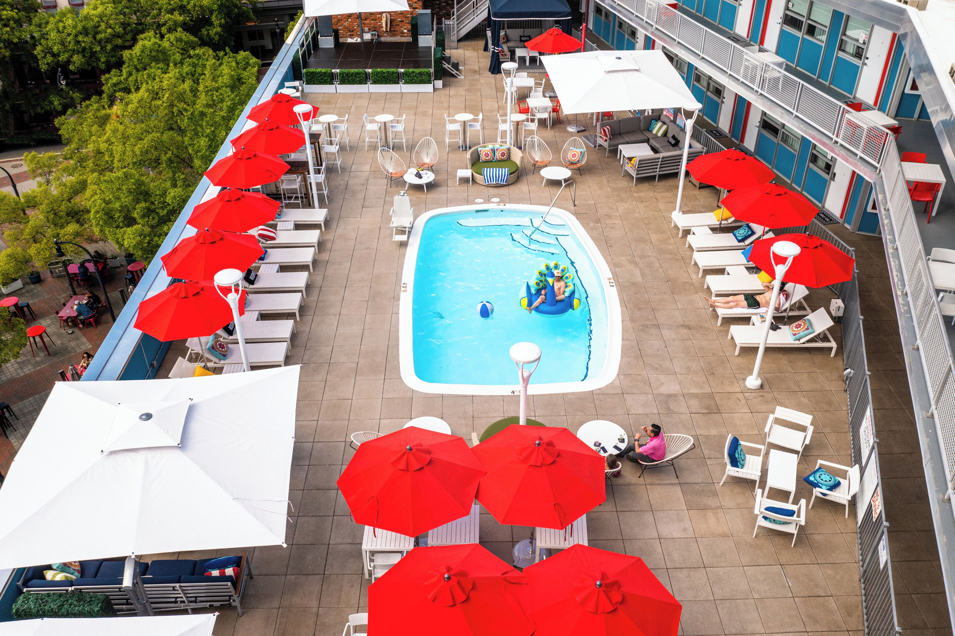 An outdoor swimming pool area with multiple red umbrellas, white lounge chairs, and a small inflatable raft.