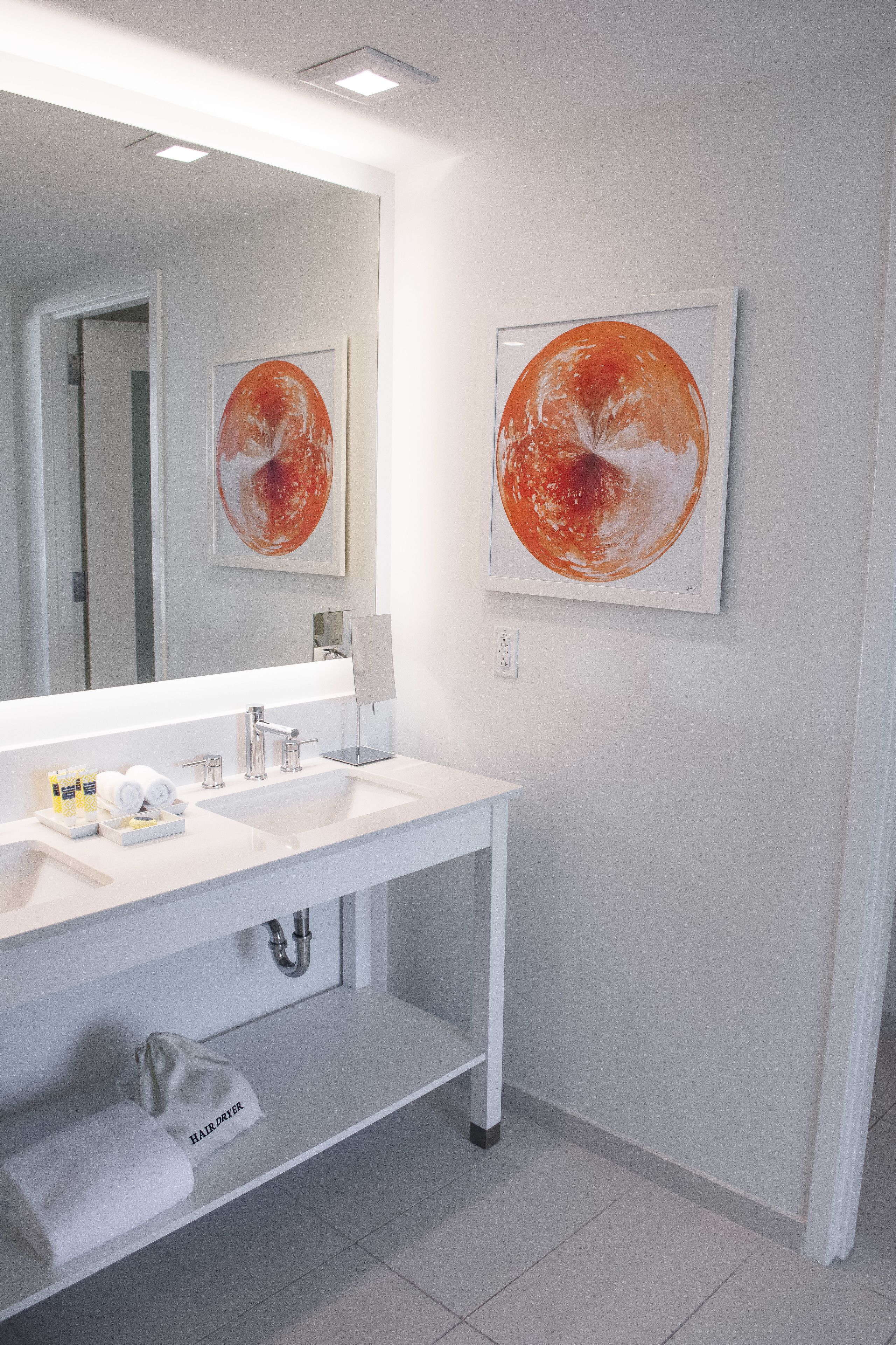 Un baño moderno con dos lavamanos, un espejo grande y una obra de arte en la pared.