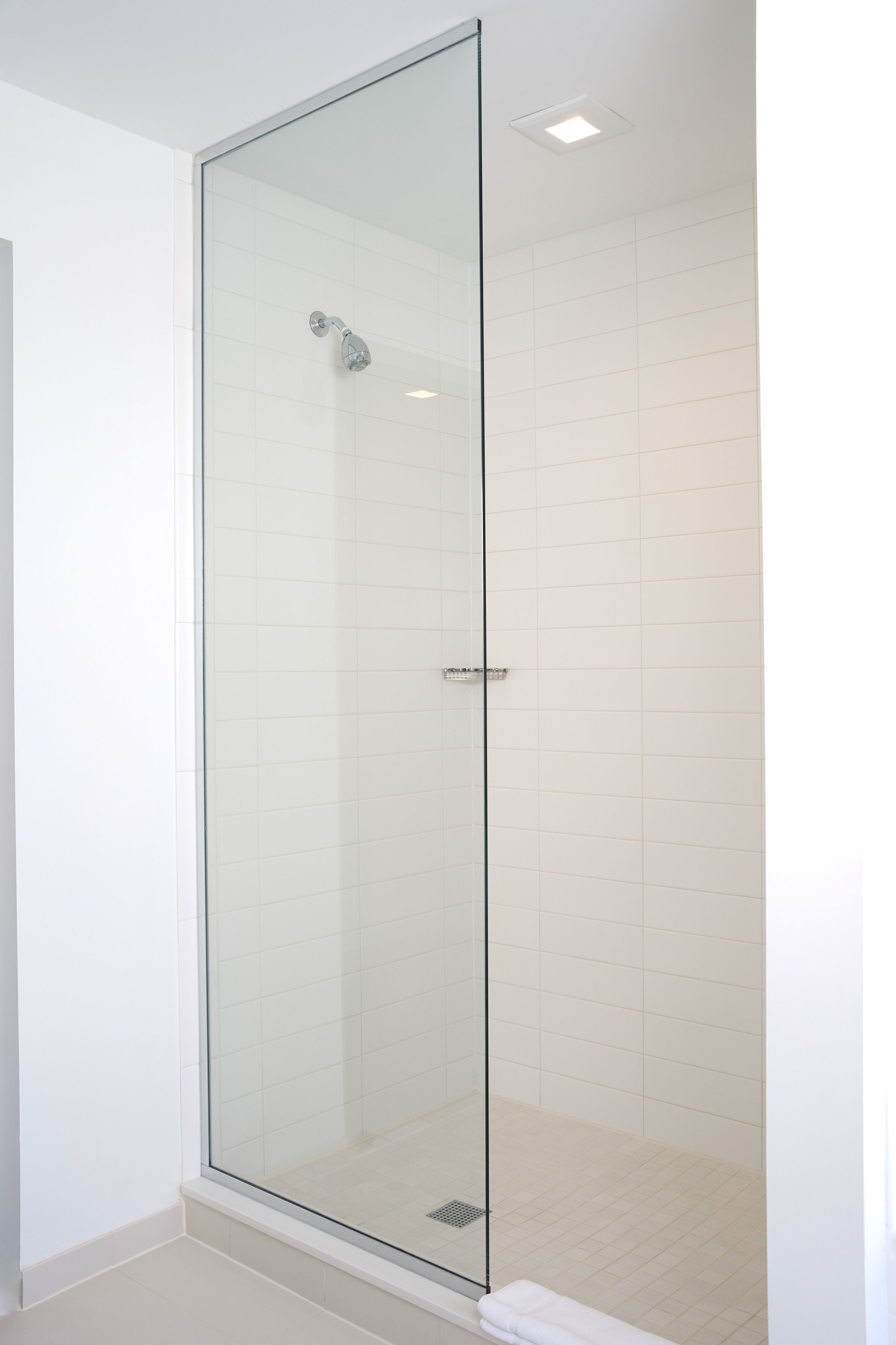 A glass-enclosed shower with white tiled walls and a white floor.
