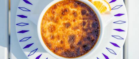 A bowl of crème brûlée on a white plate with a blue pattern, accompanied by a strawberry and an orange slice.