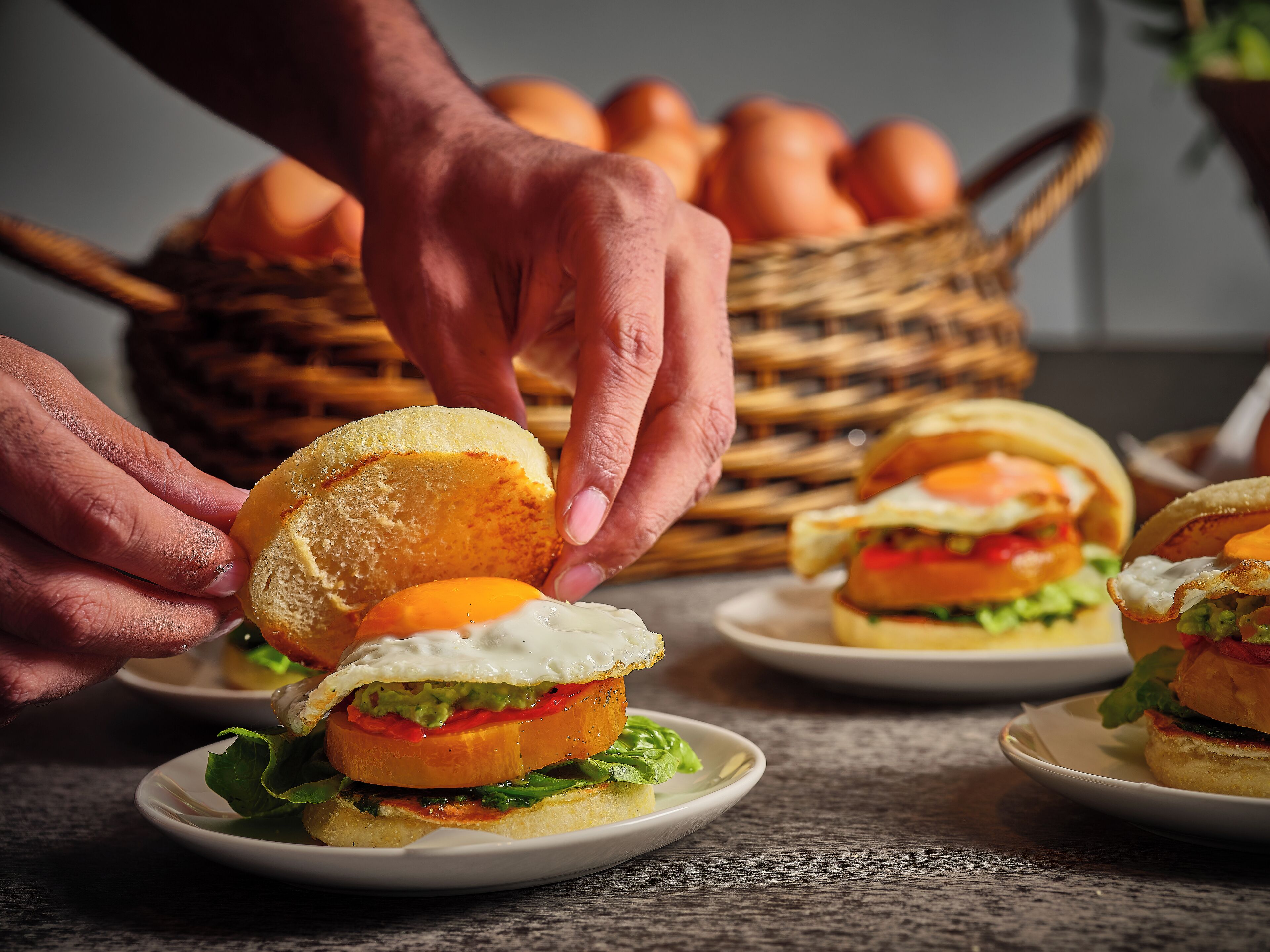 A person assembling a sandwich with a fried egg on a small plate.