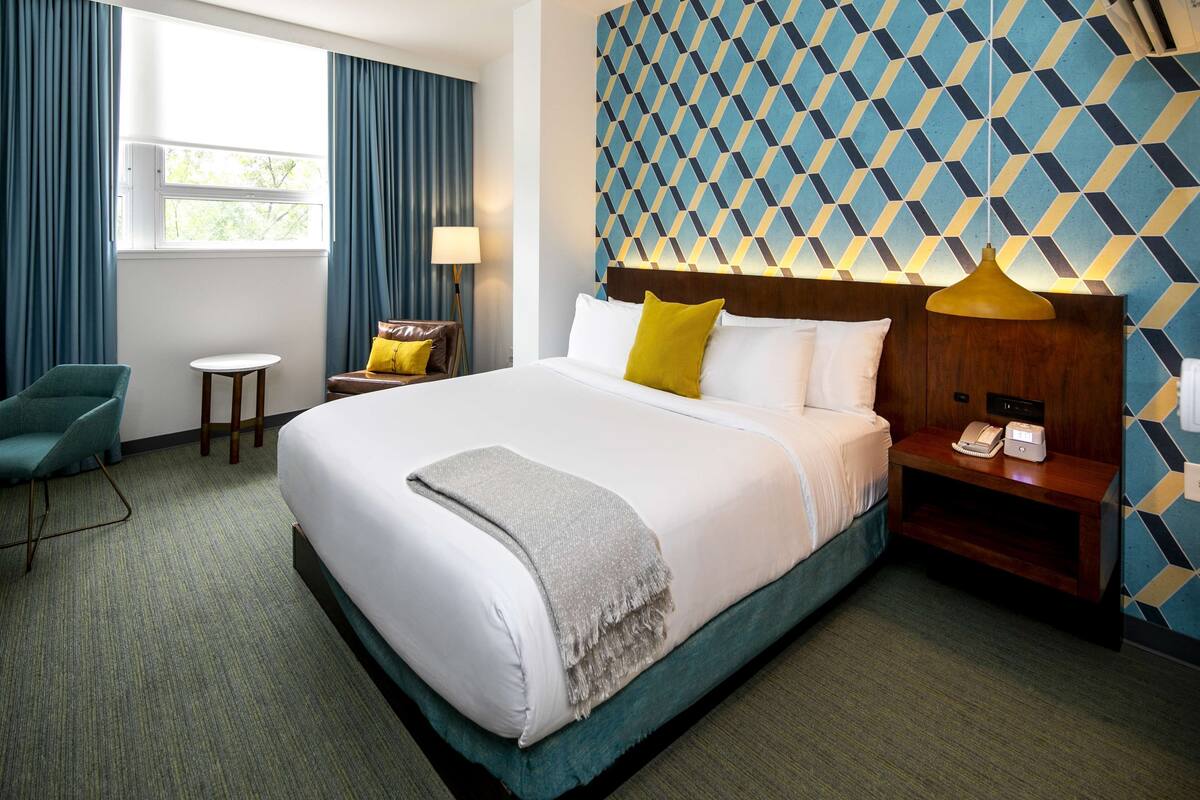 A hotel room with a large bed, a desk, a chair, and a patterned wall.