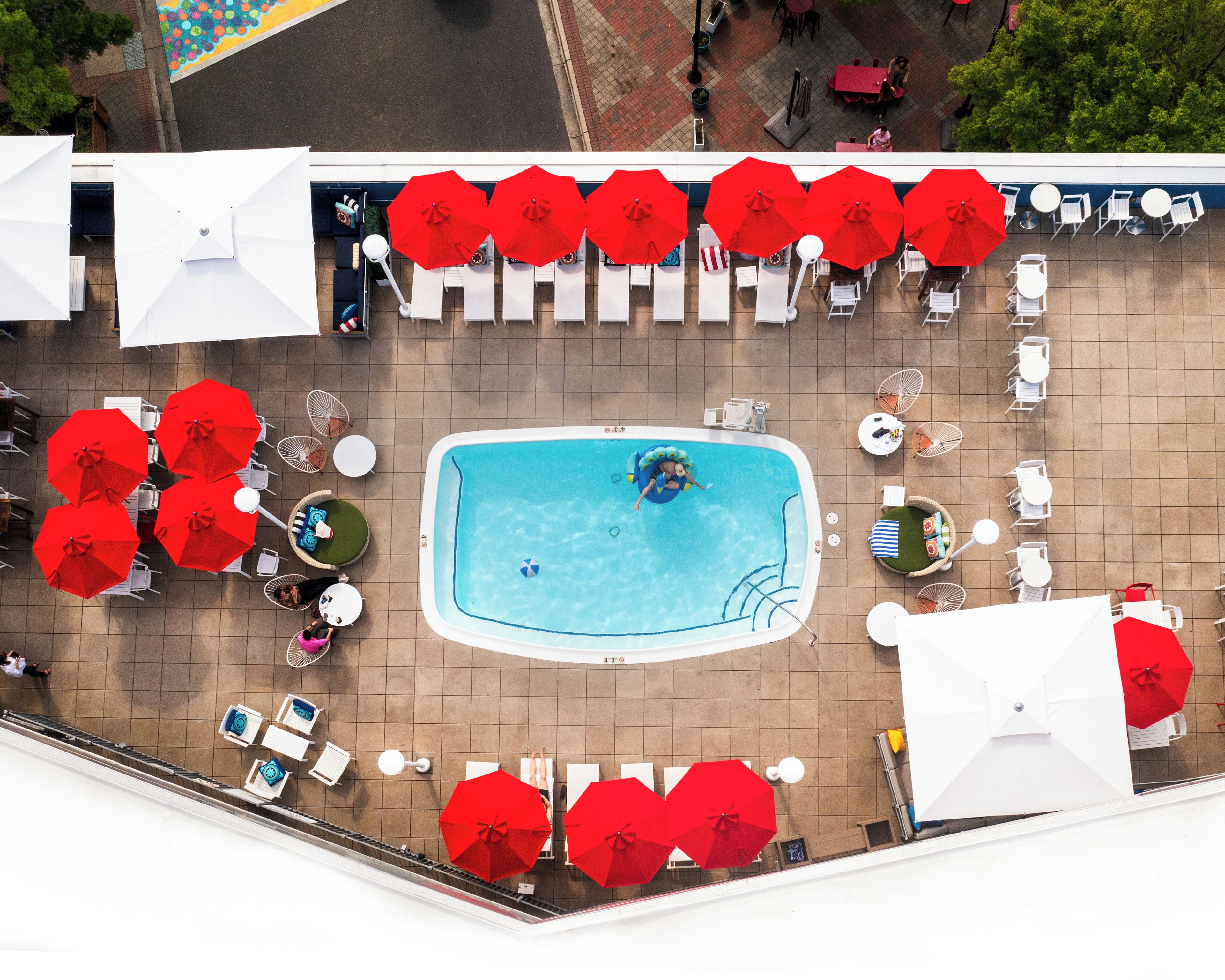 A rooftop pool area with multiple red umbrellas, white lounge chairs, and a swimming pool.