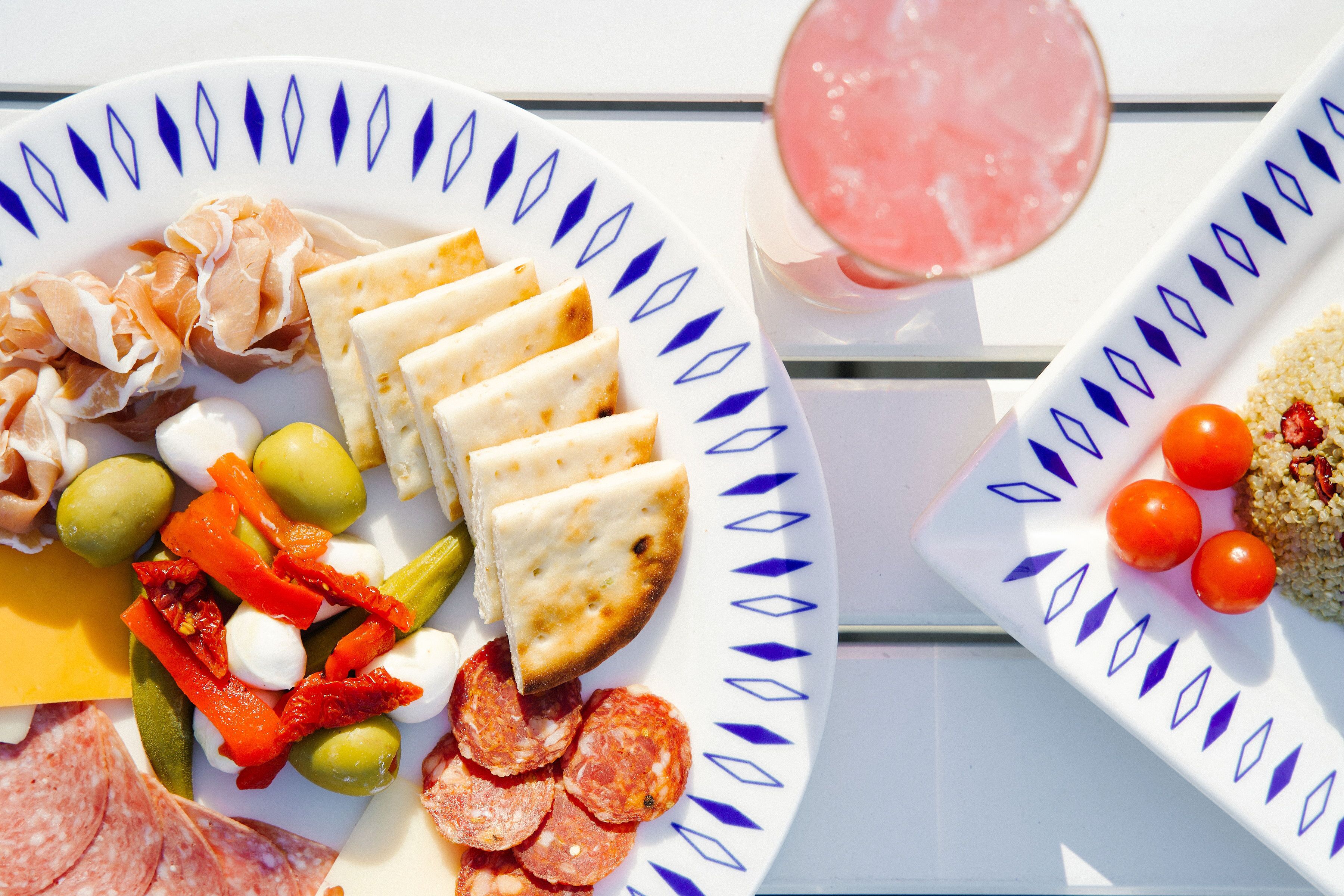 A table with a plate of cured meats, cheese, olives, and peppers.