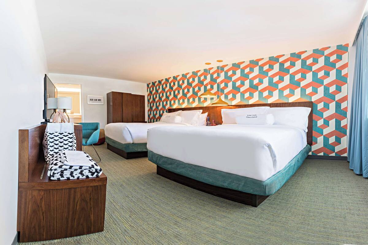 A hotel room with two beds, a wooden bench, and a patterned wall.