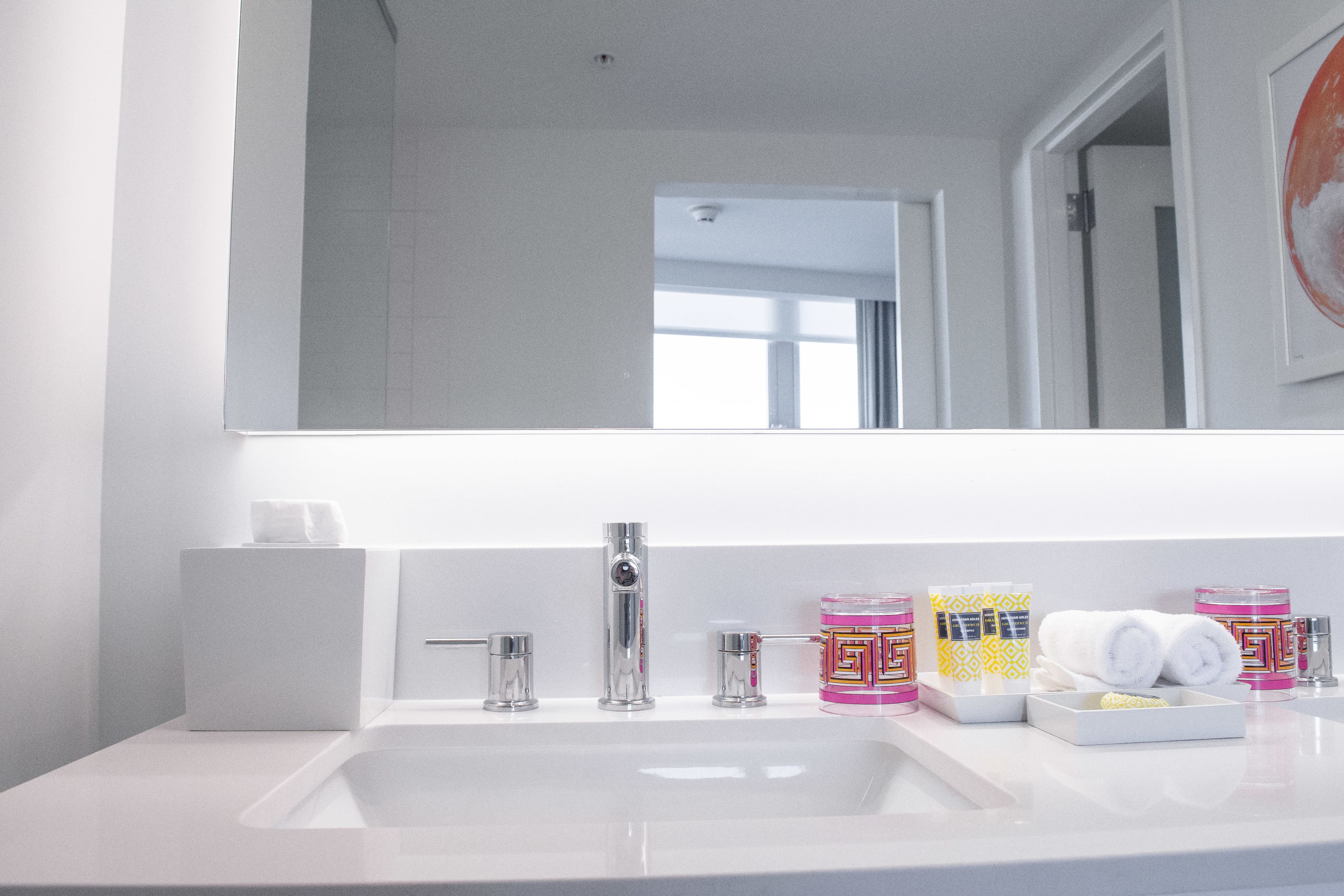 Un baño moderno con un lavamanos blanco, un espejo grande y diversos artículos de tocador sobre el mostrador.