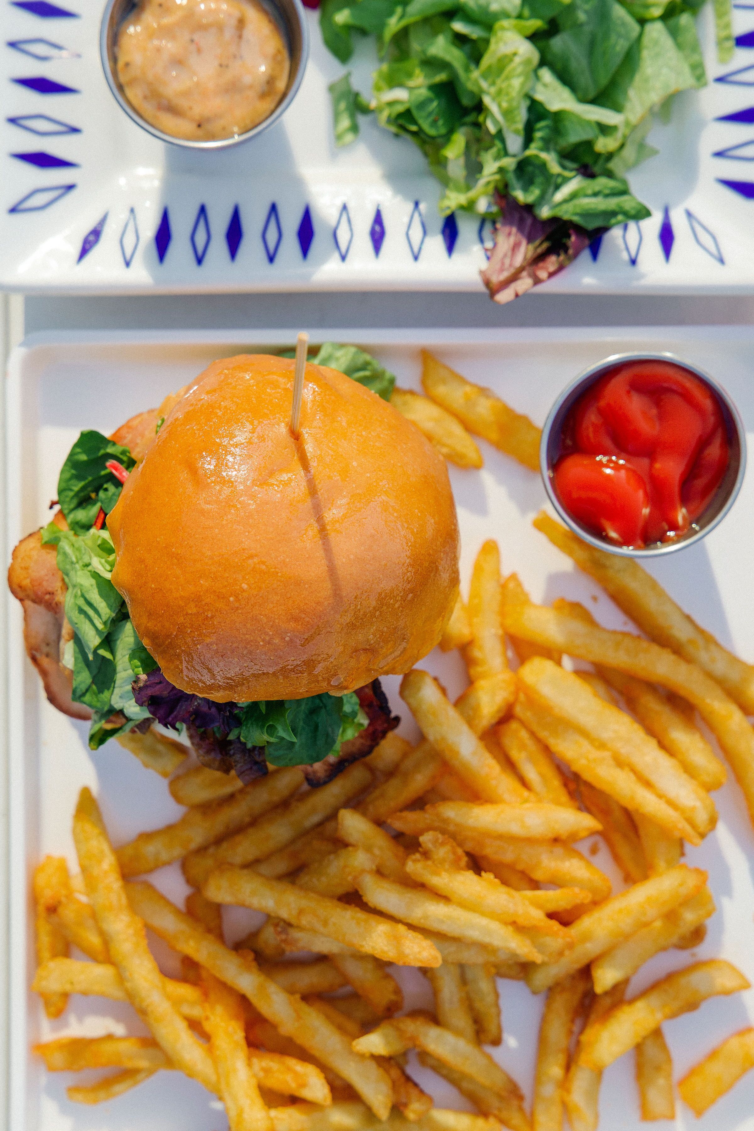 A plate with a burger, fries, and a small bowl of ketchup.