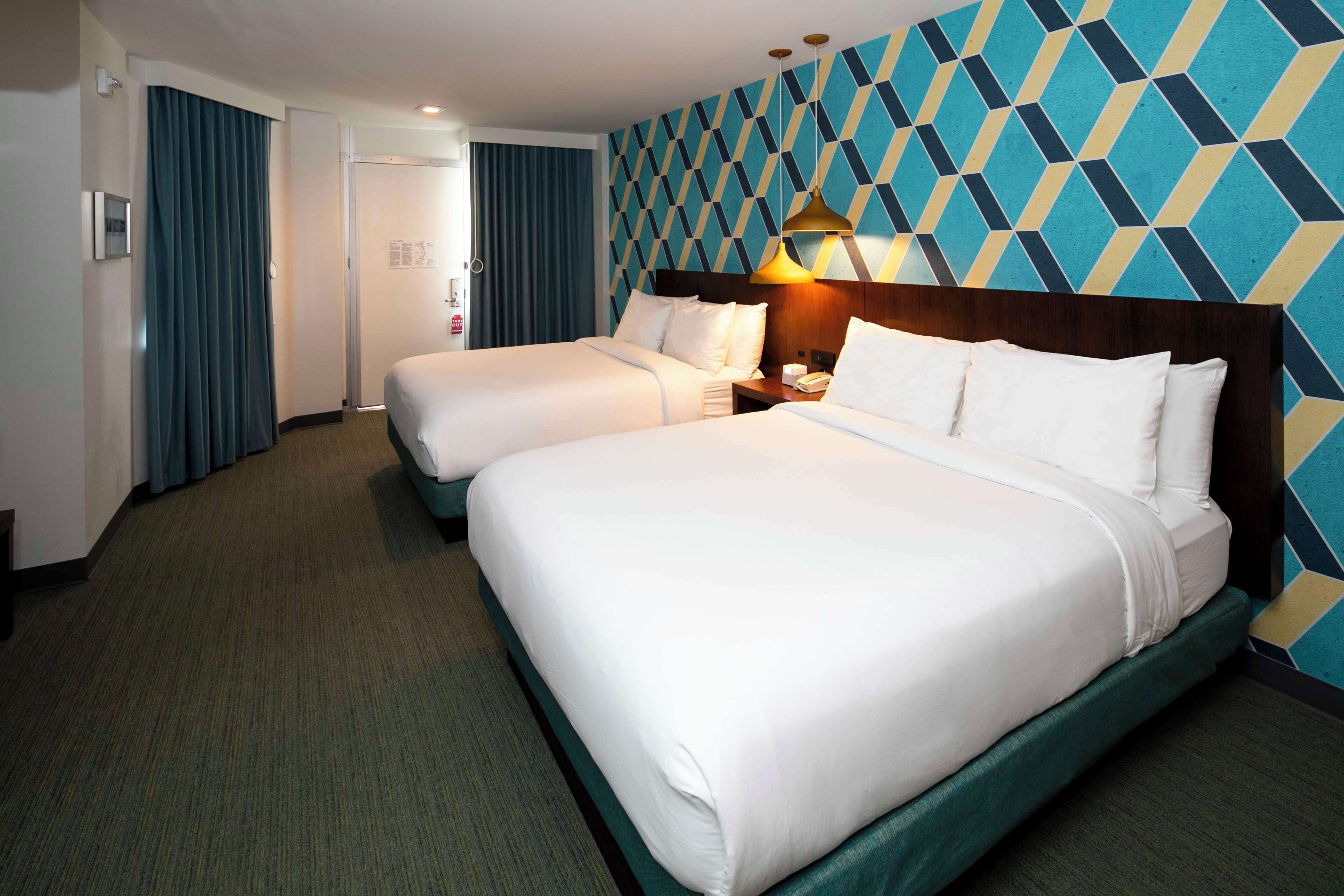 Et hotelværelse med to senge, et træhovedgærde, en tapetvæg og et tæppedæk.