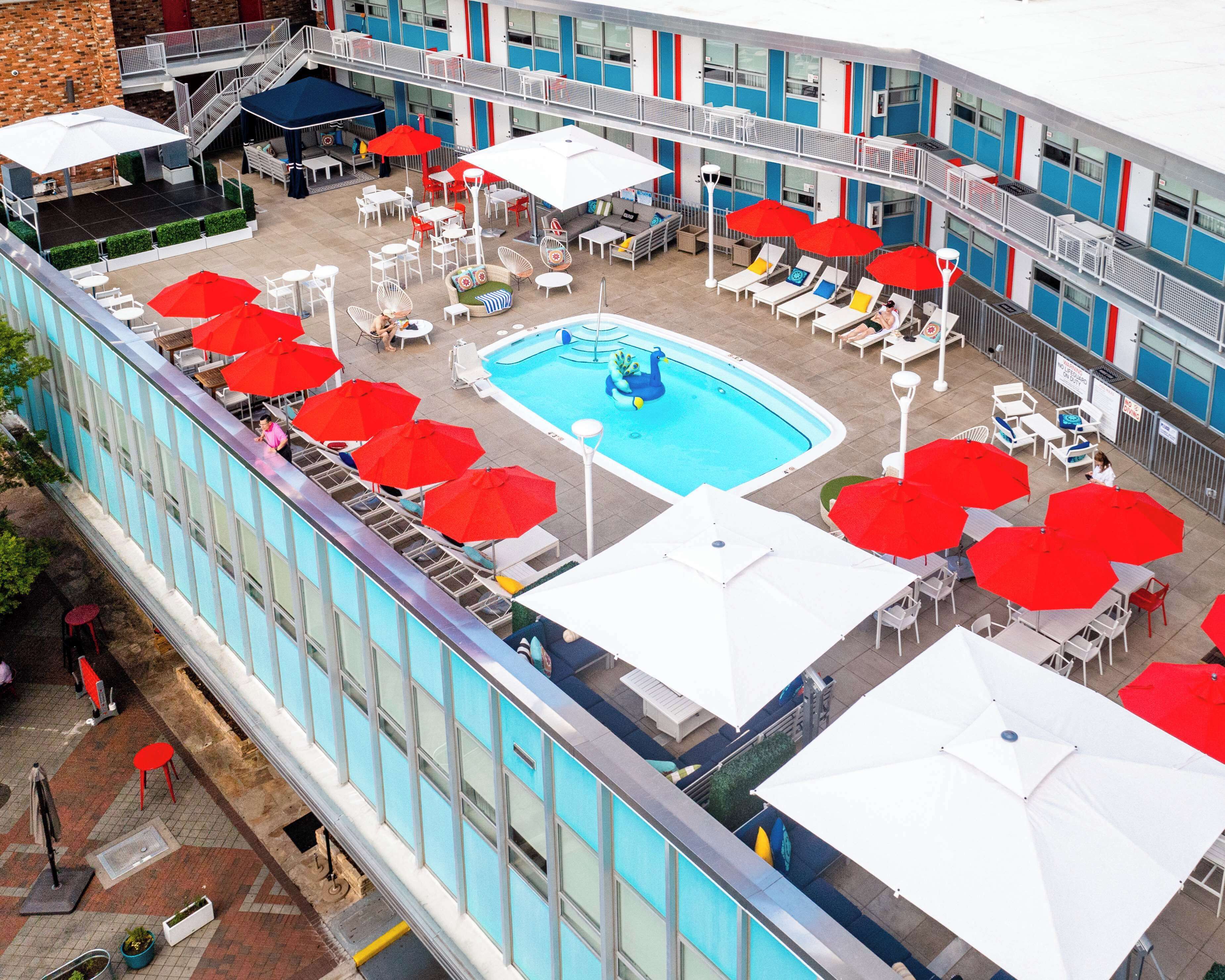 A rooftop pool area with multiple red and white umbrellas, lounge chairs, and a central pool.