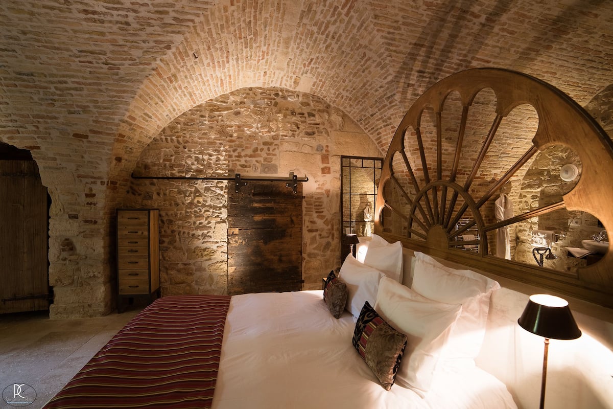 Ein Schlafzimmer mit Steinwänden, einem hölzernen Bett und einem großen Spiegel.