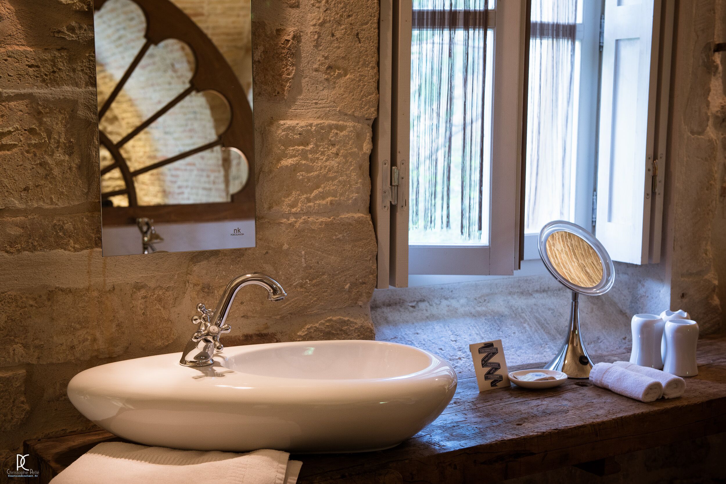 Un baño con un lavamanos blanco, un espejo y una ventana con cortinas.
