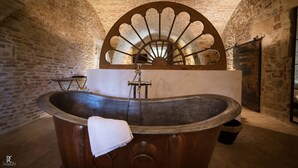 Una habitación histórica con paredes de piedra, una bañera grande y decorativa, y un abanico ornamental.