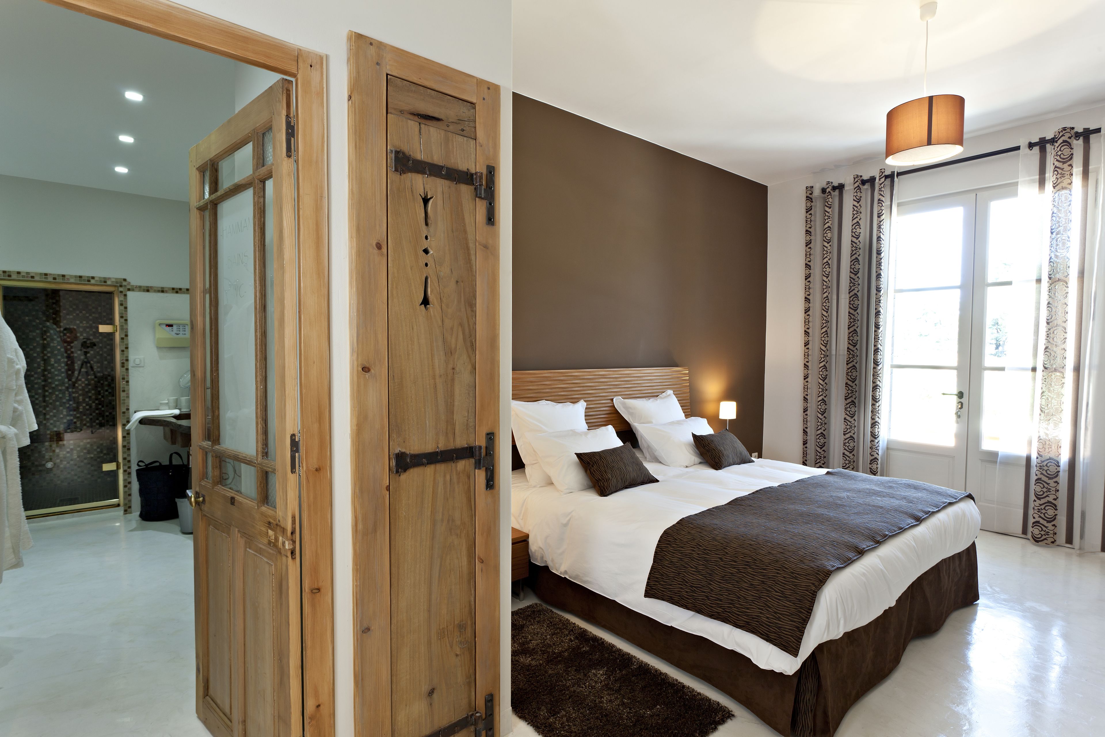 Ein Schlafzimmer mit einem großen Bett, einer Holztür und einem im Hintergrund sichtbaren Badezimmer.