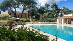 Una piscina con agua cristalina azul, rodeada de vegetación y un edificio con tejado de tejas.