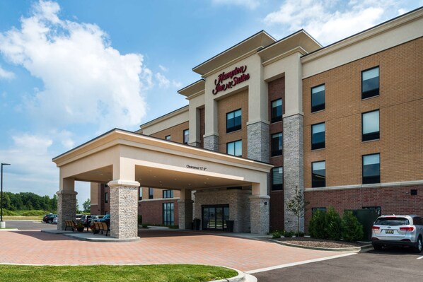 Edifício do Hampton Inn Suites com entrada coberta, área de estacionamento e fachada de tijolos.