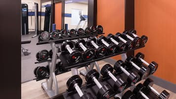 Un gimnasio con un estante de mancuernas y un espejo que refleja el interior.