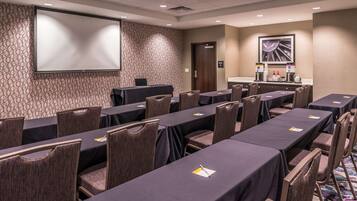 A conference room with multiple tables and chairs, a projector screen, and a coffee station.