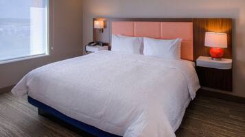 A hotel room with a large bed, a nightstand with a lamp, and a view of the city through the window.