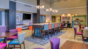 A hotel lobby with a bar area, seating arrangements, and a television. - Hampton Inn & Suites Wixom (Wixom)