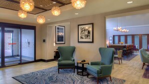 A hotel lobby with a reception desk, seating area with chairs, and a patterned rug. - Hampton Inn & Suites Wixom (Wixom)