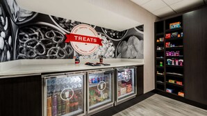 A snack bar with a 'Treats' sign, refrigerated drink dispensers, and shelves stocked with snacks and beverages. - Hampton Inn & Suites Wixom (Wixom)