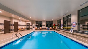 An indoor swimming pool with clear blue water, surrounded by lounge chairs and a lifeguard station. - Hampton Inn & Suites Wixom (Wixom)