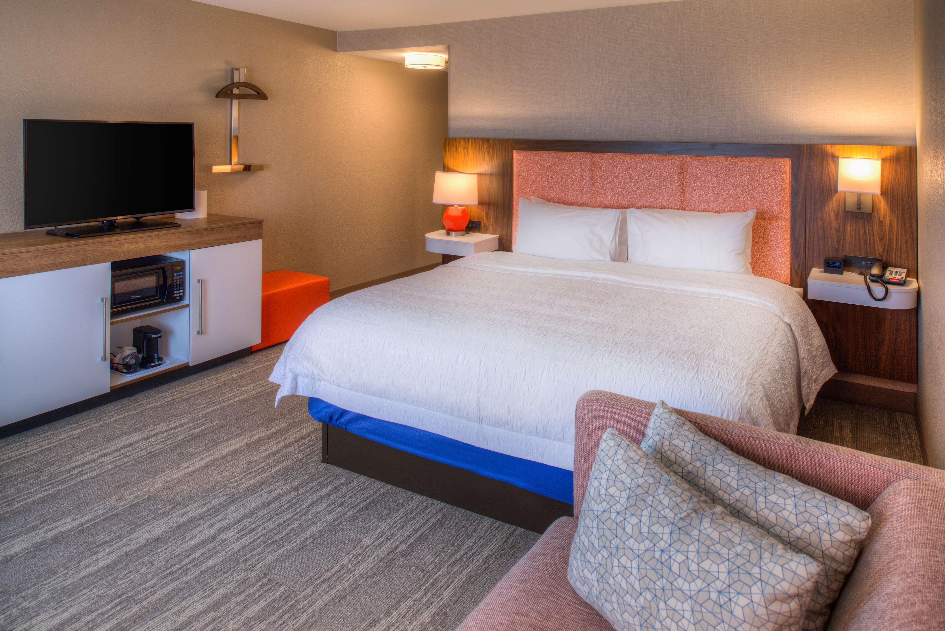 Una habitación de hotel con una cama grande, televisión, microondas y escritorio con lámpara.