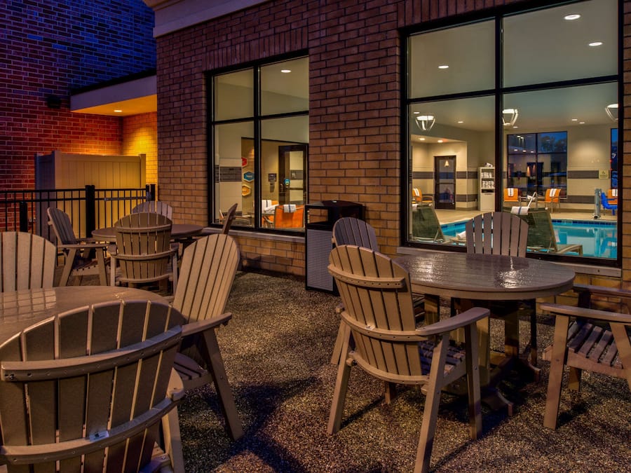 An outdoor patio area with Adirondack chairs and a table, overlooking a pool.