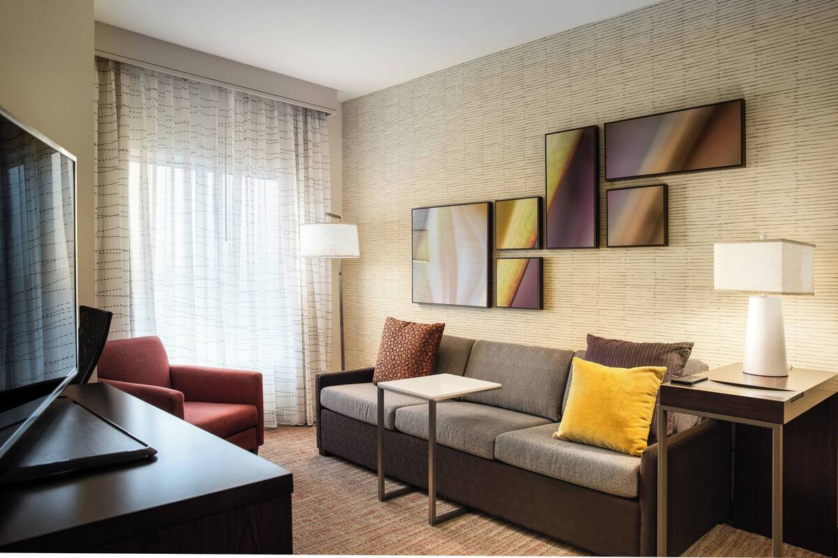 A modern hotel room with a sofa, a small table, a TV, and artwork on the wall.