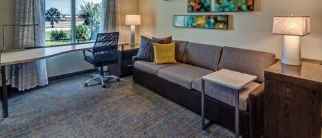 A hotel room with a large window, a sofa, a desk, and two lamps.