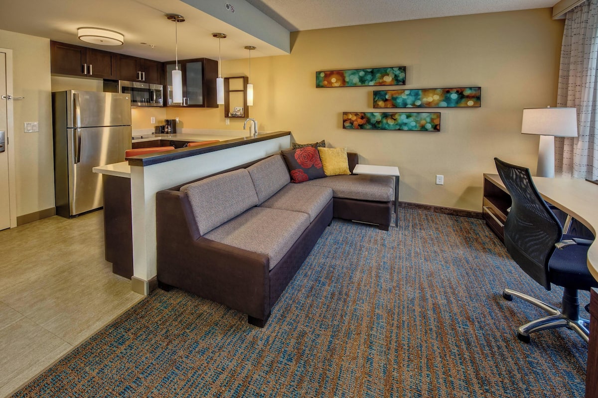 A modern hotel room with a kitchenette, a sofa, a desk, and a chair.