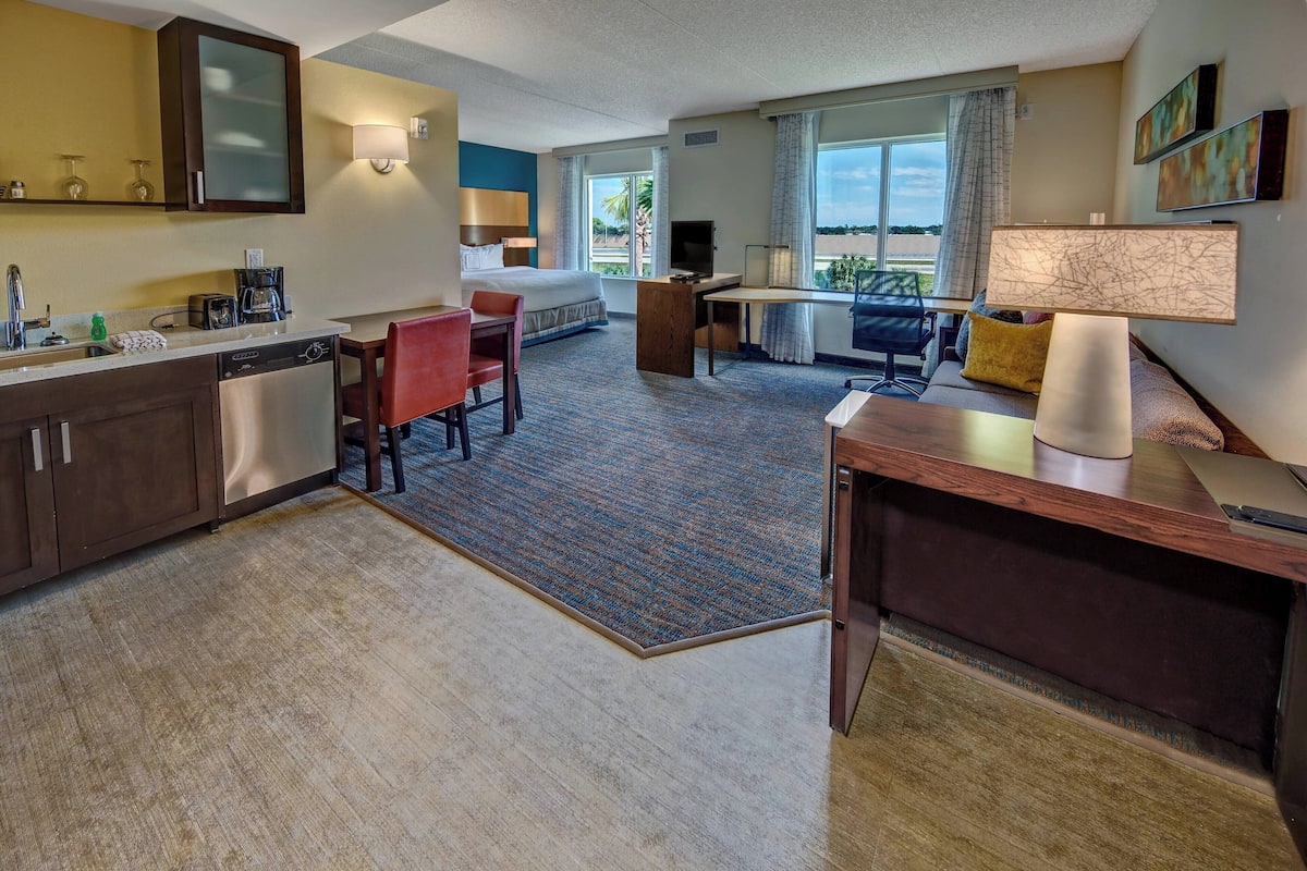 A hotel room with a bed, desk, chair, and a small kitchenette.