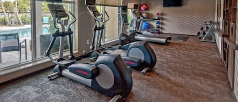 A gym with treadmills, elliptical machines, and a TV screen.
